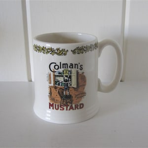 May include: White ceramic mug with a handle, featuring the text "Colman's MUSTARD" in black and red. The mug has a decorative border and a vintage illustration of a kitchen scene.