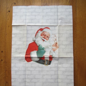 Peut inclure: Une feuille de papier rectangulaire présentant une illustration imprimée du Père Noël sur un fond de mur en briques gris clair. Le Père Noël porte un manteau rouge à bordure en fourrure blanche, une ceinture noire à boucle dorée et des moufles vertes.