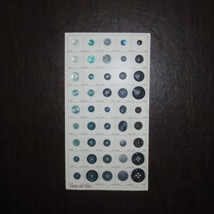 May include: A card displaying a variety of buttons in shades of blue, green, and clear. The buttons are arranged in rows and columns, with different sizes and styles. The card has the text "CARD BD-304C" printed on it.