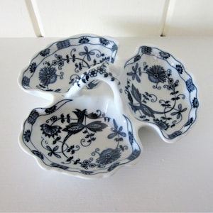 May include: White ceramic serving dish with three sections, featuring a blue floral pattern. The dish has a handle and a scalloped edge. The design includes flowers, leaves, and vines. A decorative piece for serving snacks or appetizers.