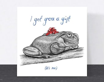May include: A white card with a hand-drawn illustration of a frog wearing a red bow. The text on the card reads "I got you a gift (It's me)."
