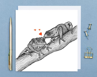 May include: A black and white illustration of two frogs on a branch. The frog on the left is looking at the frog on the right, who is kissing the other frog on the head. There are small red hearts floating in the air between the frogs.