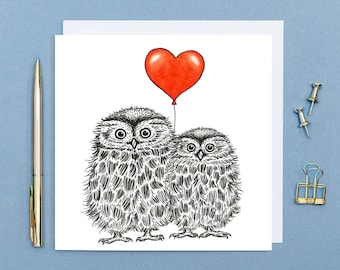 Può includere: Un biglietto d'auguri con un'illustrazione in bianco e nero di due gufi con un palloncino rosso a forma di cuore. I gufi guardano lo spettatore.