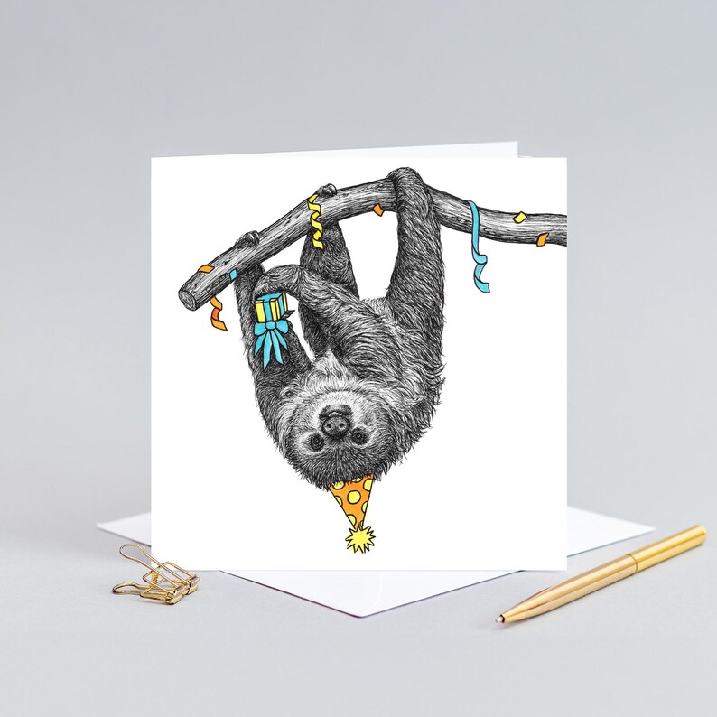 May include: A birthday card featuring a black and white illustration of a sloth wearing a party hat and holding a gift, hanging upside down from a branch with colorful streamers.