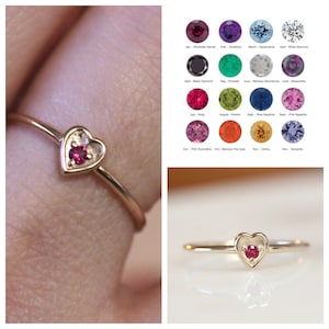 May include: A gold heart-shaped ring with a small red gemstone in the center.