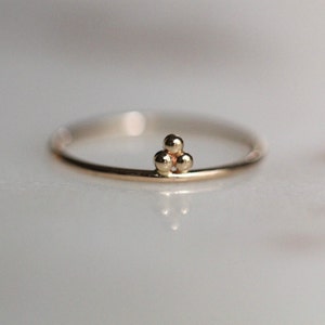 May include: A delicate gold ring with a cluster of three small, round beads in the center.