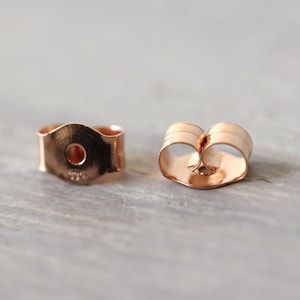 May include: Two gold-toned earring backs. One is a standard butterfly back, the other is a flat back with a small hole in the center.