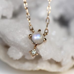 May include: A delicate gold necklace featuring a round moonstone pendant with a small diamond accent. The necklace is displayed against a white background.