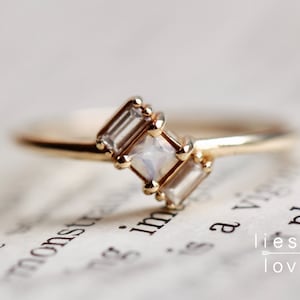 May include: A gold ring with three clear rectangular gemstones. The center stone is larger than the two stones on either side.