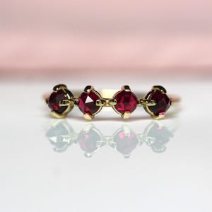 Könnte beinhalten: Ein goldener Ring mit vier roten Edelsteinen in einer Reihe. Die Edelsteine sind tiefrot und der Ring hat eine polierte Oberfläche. Das Design ist schlicht und elegant, geeignet für den täglichen Gebrauch.