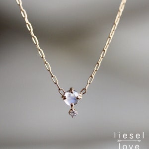 May include: A delicate gold chain necklace featuring a small, clear moonstone pendant with a tiny diamond accent.