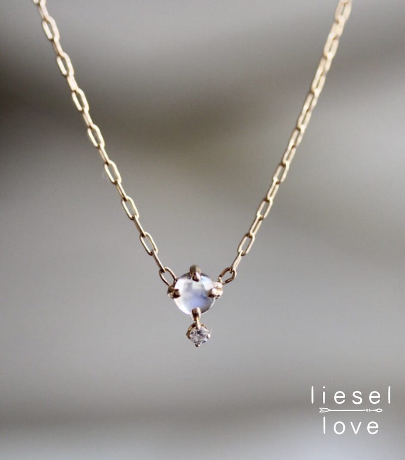 May include: A delicate gold chain necklace featuring a small, clear moonstone pendant with a tiny diamond accent.