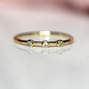 Puede incluir: Un delicado anillo de banda de oro con tres pequeños diamantes redondos engastados en fila.