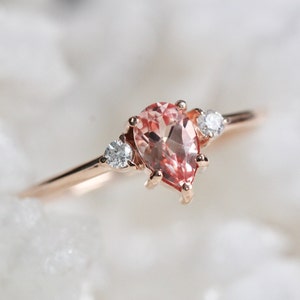 Op de afbeelding: Een ring van roségoud met een peervormige roze edelsteen en twee kleinere ronde, heldere edelstenen.