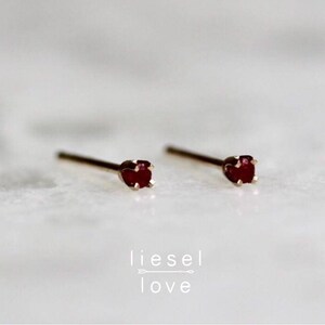 May include: A pair of small, gold stud earrings with a single, dark red gemstone in each.