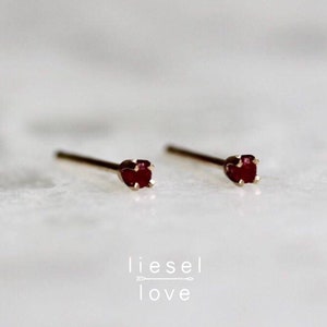 May include: A pair of gold stud earrings with small red gemstone accents. The earrings are simple and elegant.
