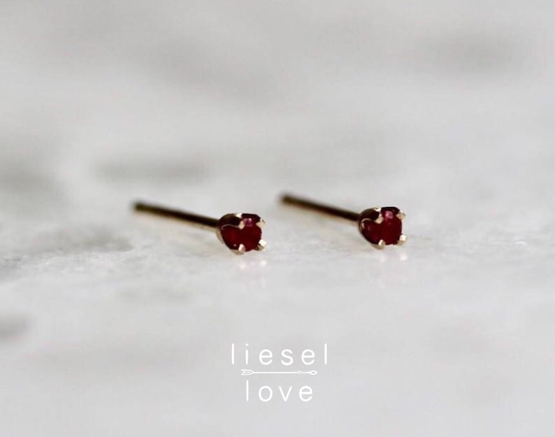 May include: A pair of gold stud earrings with small red gemstone accents. The earrings are simple and elegant.
