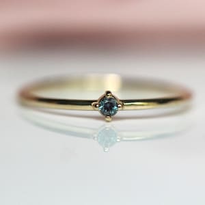 May include: A delicate gold band ring with a small, round, blue gemstone set in the center.