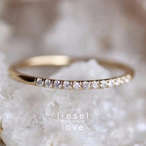 May include: A delicate gold band ring with a row of small diamonds set along the top. The ring is simple and elegant.