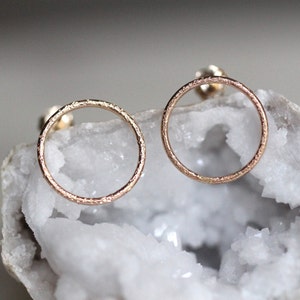 May include: A pair of rose gold circle earrings with a textured finish. The earrings are simple and elegant, and would make a great gift for any occasion.