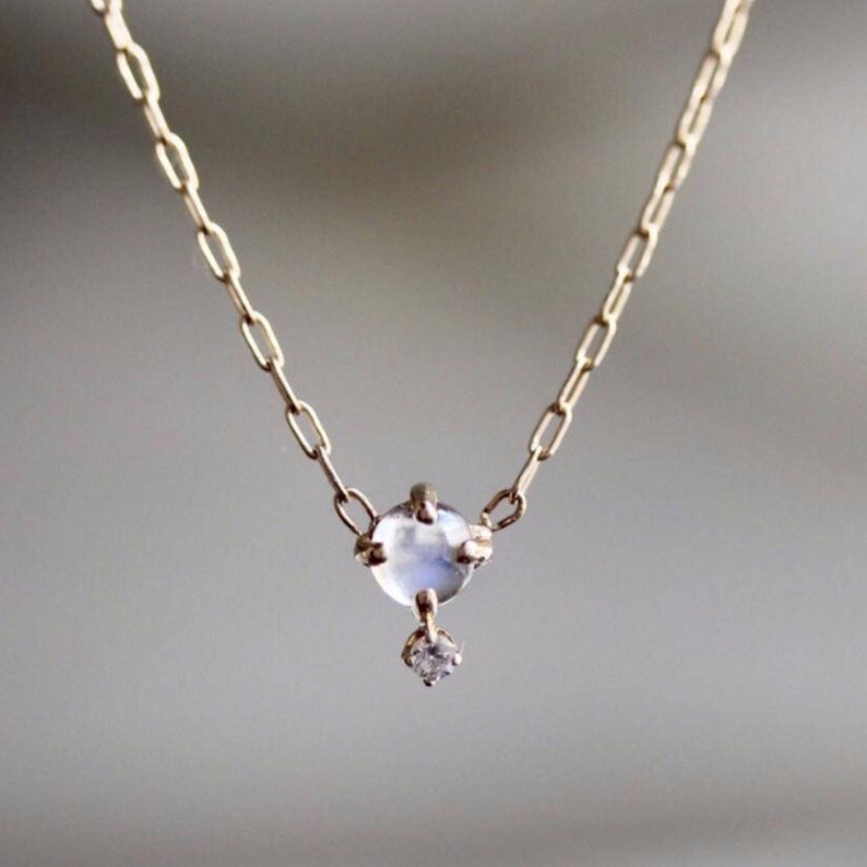 May include: A delicate gold chain necklace featuring a moonstone pendant with a smaller diamond accent.