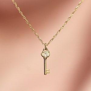 May include: A gold key necklace with a clear diamond-shaped stone in the keyhole. The chain is a delicate, linked style.