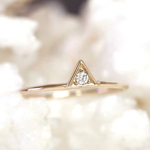 May include: A delicate gold ring with a small diamond set in a triangle shape.