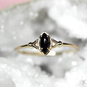 May include: A gold ring with a black marquise-shaped gemstone set in a delicate, geometric design.