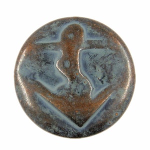 May include: A round ceramic tile with a copper glaze and a raised anchor design. The anchor is a dark brown color and the glaze has a blue-green color.