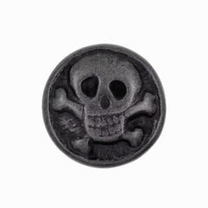 Op de afbeelding: Een ronde, donkergrijze knoop met een schedel en gekruiste botten. De schedel heeft zichtbare oogkassen, een neusholte en een rij tanden. De gekruiste botten zijn eronder geplaatst, een klassiek piratenthema.