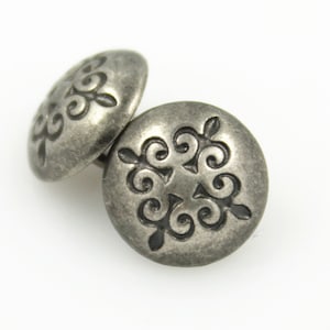 May include: Two silver metal buttons with a decorative, ornate design. The buttons have a raised, circular design with a swirl pattern.