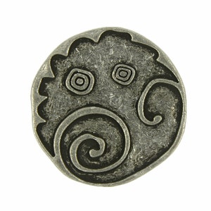 May include: A silver-toned metal charm with a circular design featuring a stylized face with swirling patterns.