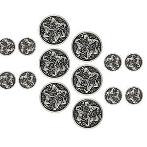 Puede incluir: Doce botones de metal plateados con un diseño de nudo celta. Cada botón tiene una forma circular con un diseño en relieve de cuatro nudos entrelazados.