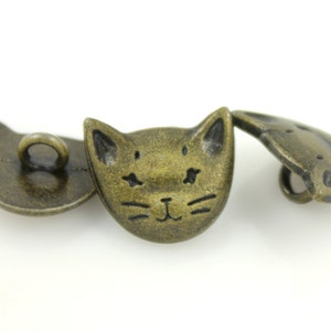 May include: Three antique gold-toned metal buttons with a cat face design. The buttons have a hole for sewing.