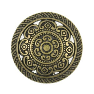 Puede incluir: Un botón redondo de metal de color dorado antiguo con un diseño decorativo intrincado. El botón tiene un patrón circular calado con un círculo más pequeño en el centro.