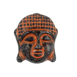May include: A small, orange and black ceramic sculpture of a Buddha head. The sculpture has a detailed face with closed eyes and a serene expression.