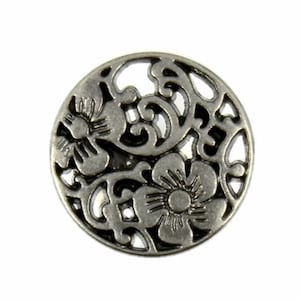 Puede incluir: Botón de metal plateado con un diseño floral. El botón es redondo y tiene un diseño recortado que se asemeja a flores y enredaderas.