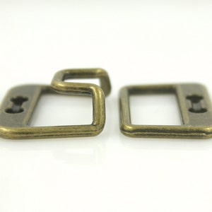 May include: Two antique gold metal belt buckle loops. The loop on the left has a curved, open end. The loop on the right has a straight, closed end.