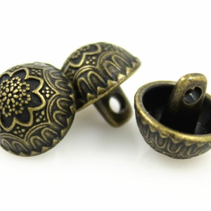 May include: Three antique gold-toned buttons with intricate floral designs. The buttons have a domed shape and a shank on the back for sewing.