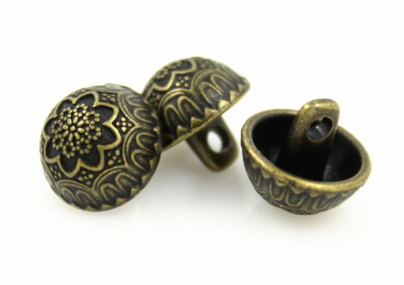 May include: Three antique gold-toned buttons with intricate floral designs. The buttons have a domed shape and a shank on the back for sewing.