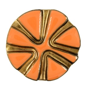 Op de afbeelding: Een ronde, oranje en goudkleurige broche. De broche heeft een helderoranje emaille centrum met goudkleurige metalen accenten. Het ontwerp heeft een geometrisch patroon met gebogen lijnen en een glanzende afwerking.