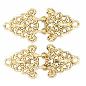 May include: Two gold-toned metal decorative clasps with intricate filigree designs. Each clasp has two loops on either side for attaching to fabric.