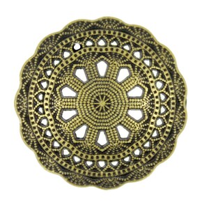 Könnte beinhalten: Ein runder, goldfarbener Metallschmuck mit einem dekorativen, filigranen Design. Der Schmuck hat ein kreisförmiges, durchbrochenes Muster mit einem kleineren Kreis in der Mitte.