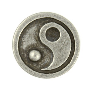 May include: A silver-toned metal charm with a yin yang symbol design. The symbol is in black and white and has a textured surface.