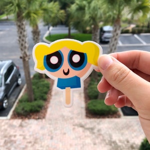 May include: A sticker of a cartoon character with blonde hair, blue eyes, and a blue shirt. The character is holding a popsicle.