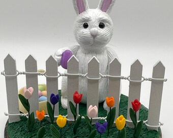 Handmade clay Easter Bunny hiding eggs in tulips.