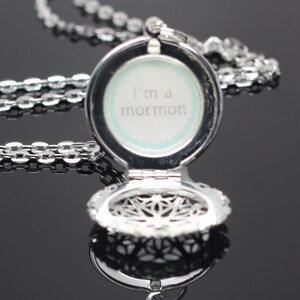 May include: Silver locket necklace with a filigree design. The locket is open and reveals a white background with the text "i'm a mormon" written in black.