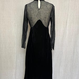 以下が含まれることがあります： 黒いベルベットのドレス。長袖とレースのバックデザイン。ドレスはハイネックで、スカートは流れるようなシルエット。レースのバックは精巧なディテール。マネキンに着せられています。