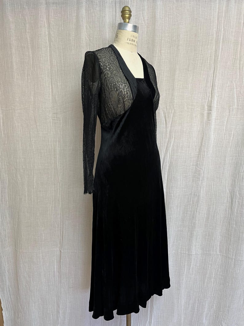 以下が含まれることがあります： 黒いベルベットのドレスと、透け感のあるレースのボレロジャケット。 ドレスはスクエアネックで、スカートは流れるようなデザインです。 ボレロは長袖で、繊細なレースのディテールが特徴です。 ドレスはマネキンに着せられています。