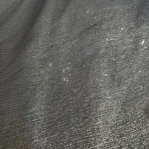 以下が含まれることがあります： 細い水平線が入った、質感のある濃い灰色の生地のクローズアップ。生地はわずかに光沢があり、表面には小さな明るい色の斑点が散らばっています。全体的な外観は織り込まれた素材です。